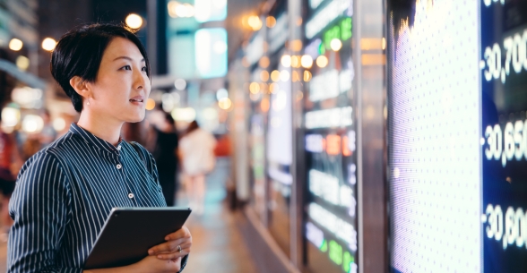 Woman with iPad looks at financial information displayed on a screen