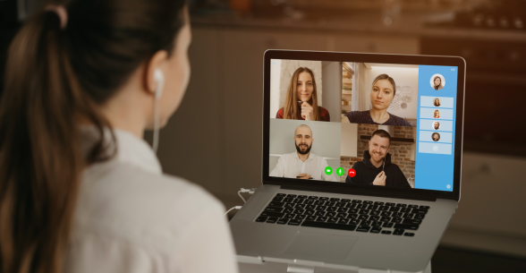 A young lady looks at the screen of her laptop which is displaying the faces of people she is videoconferencing with