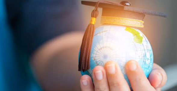 A hand hold a baseball-size earth that has a graduation cap on top