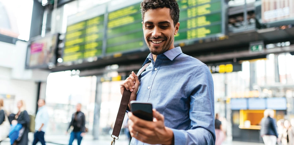 Image of a man in business attire looking at his phone and smiling while in an airport.