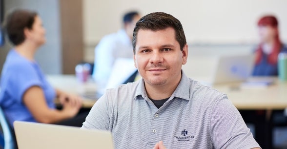 Image of an Accelerated Master of Applied Leadership and Management student smiling at a laptop in a classroom located in Thunderbird School of Global Management's Global Headquarters.