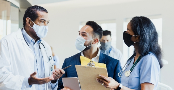Image of three diverse healthcare professionals wearing masks in a hospital setting holding clipboards.