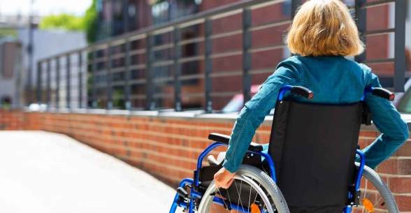 A woman in a wheelchair prepares to take a ramp to enter a building.