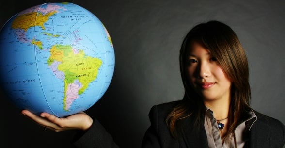 An Asian woman holds a globe in her hand.