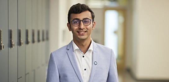 Image of a Thunderbird student in a suit smiling at the camera in front of lockers.